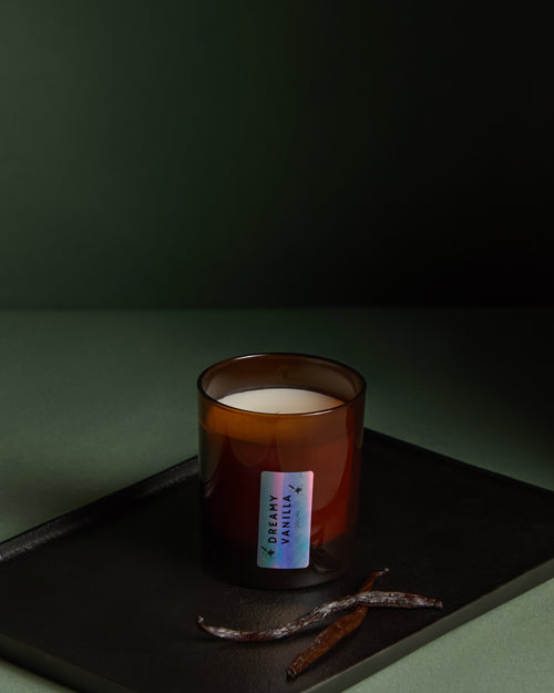 Candle in an amber glass jar with a label on a dark surface