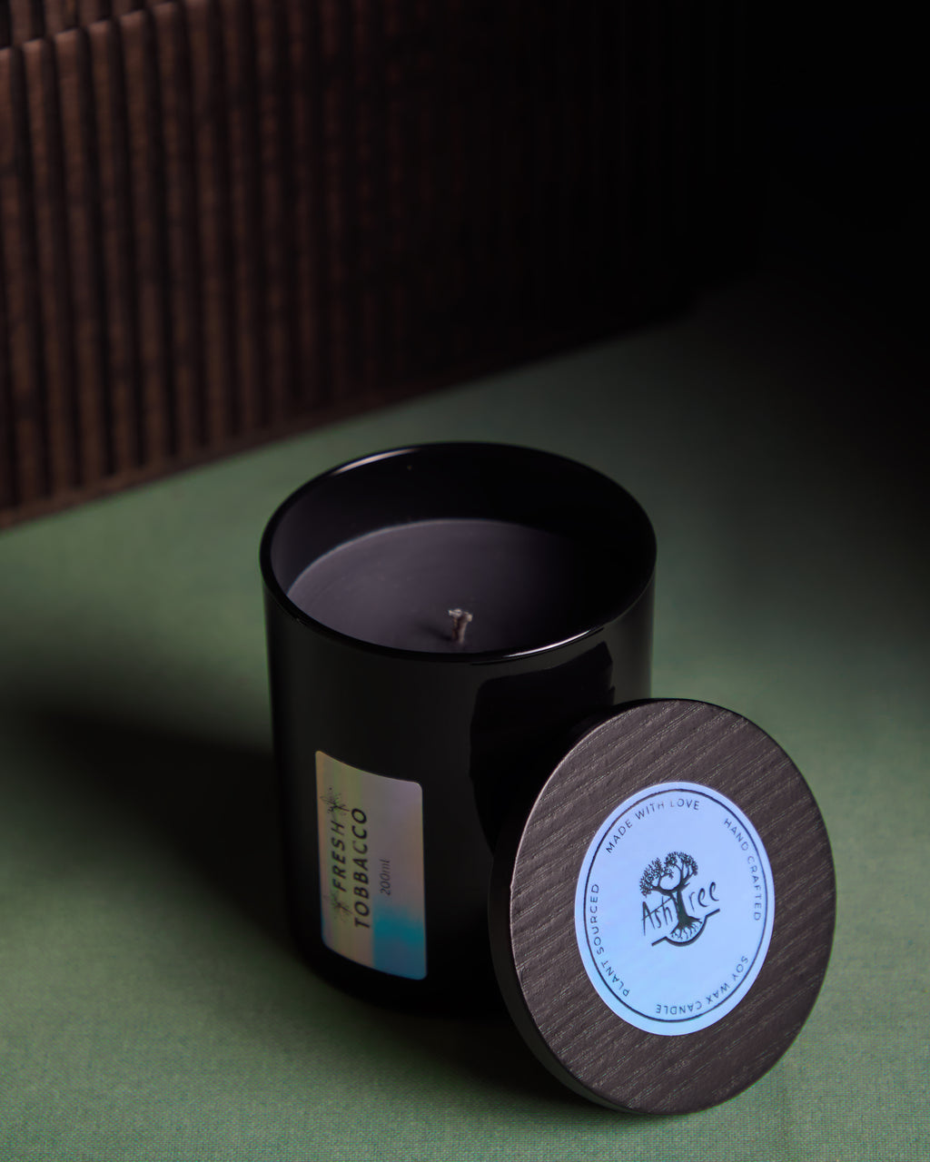 Black candle with wooden lid on a green surface