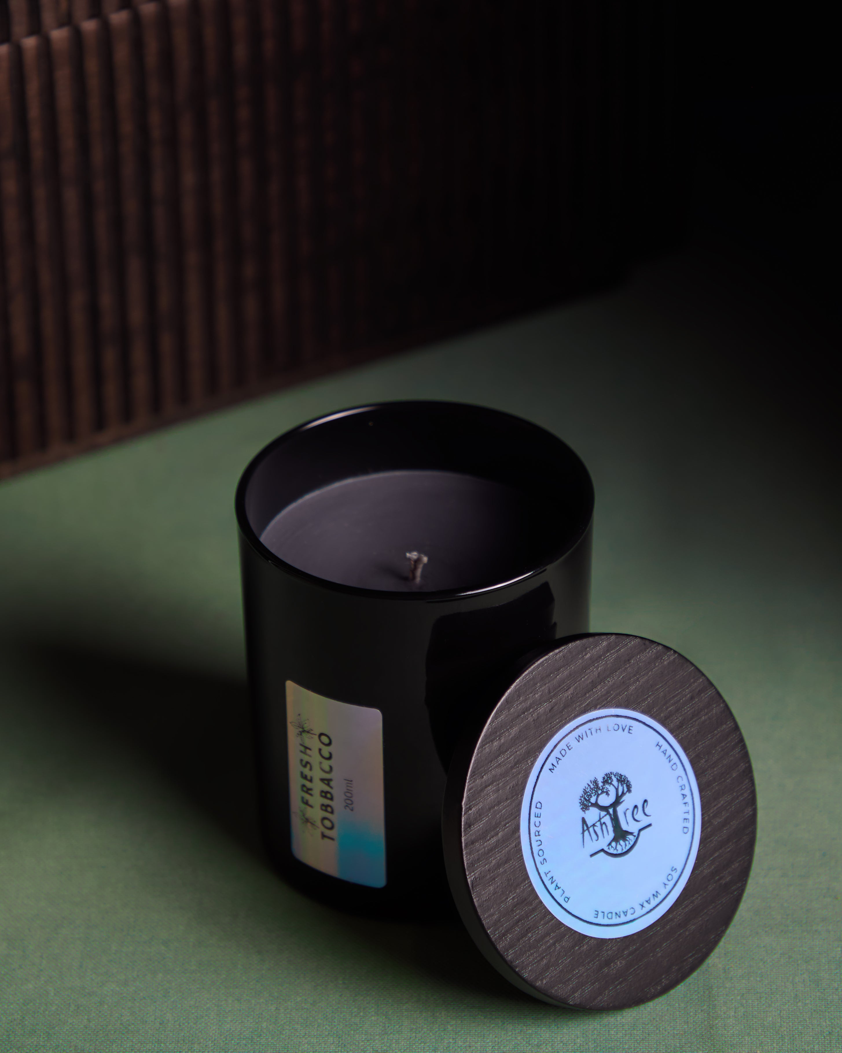 Black candle with wooden lid on a green surface