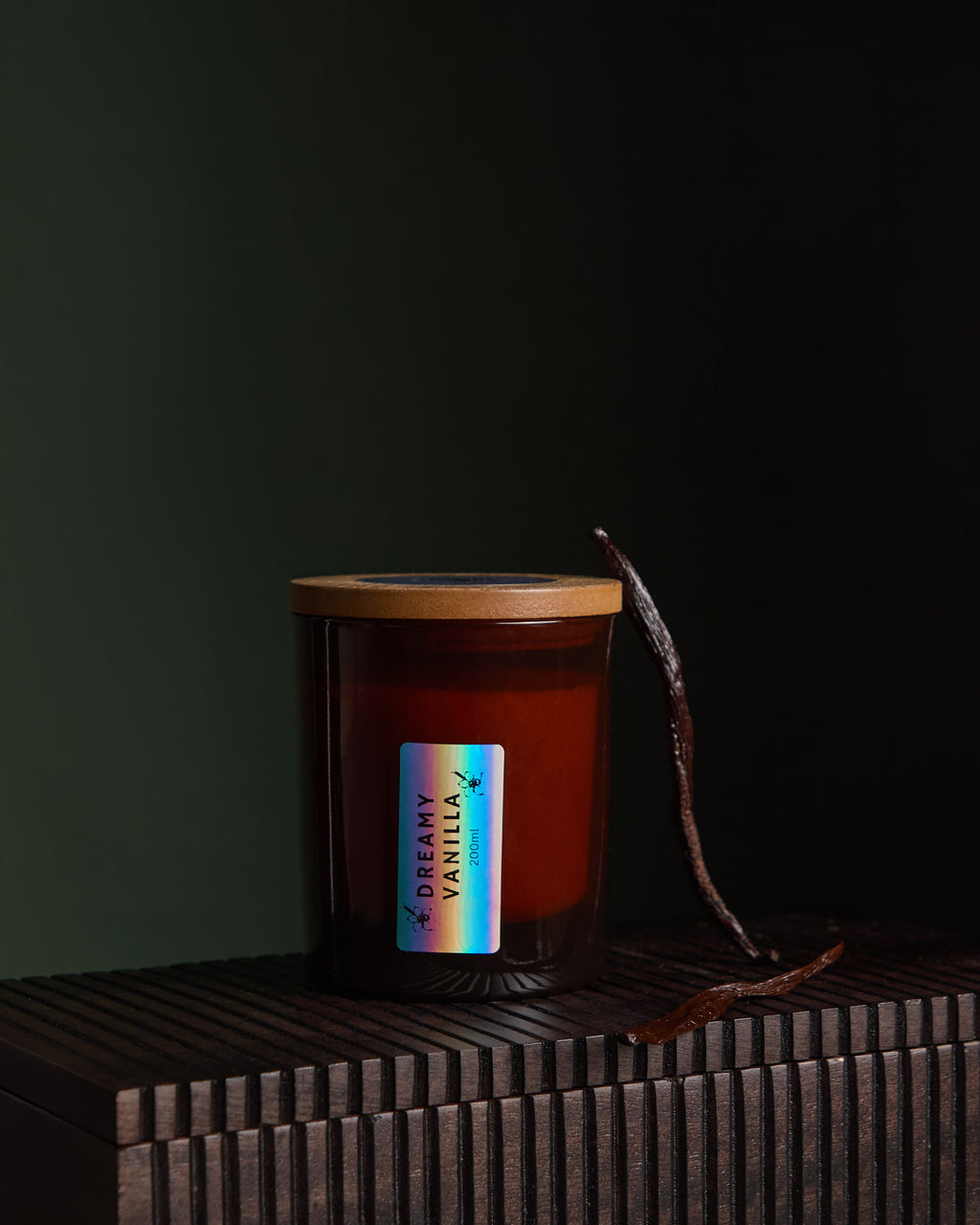 Side view of Luxury hand poured soy wax candle with natural soy wax colour in an amber glass jar, wooden lid and fabric wick, finished with holographic silver label