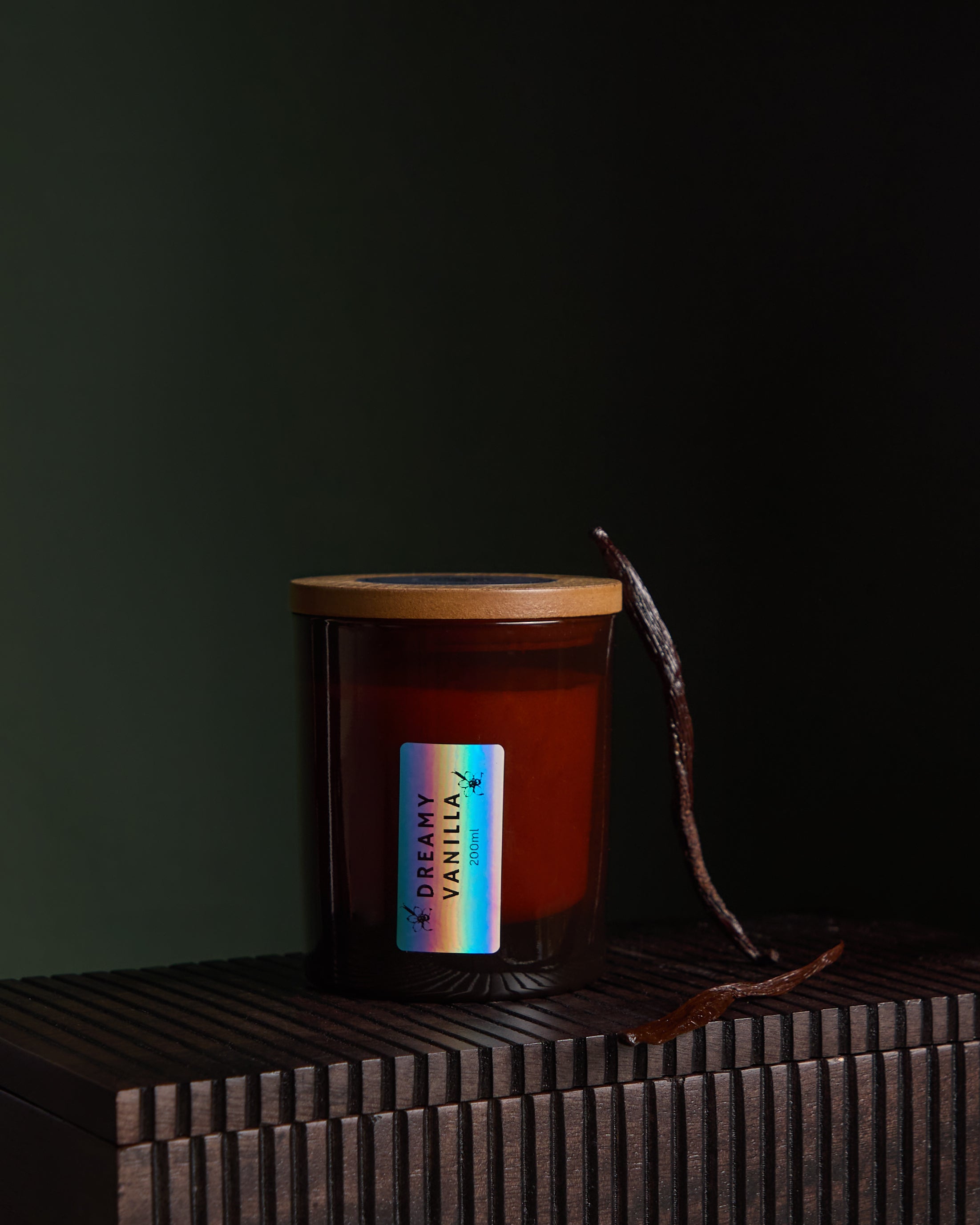 Side view of Luxury hand poured soy wax candle with natural soy wax colour in an amber glass jar, wooden lid and fabric wick, finished with holographic silver label