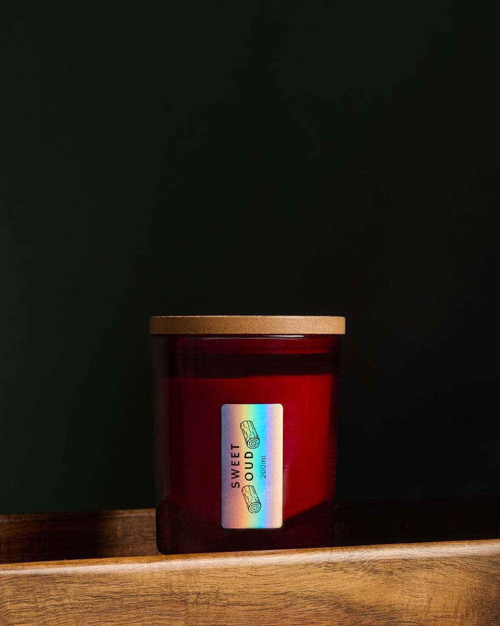 Side view of Luxury hand poured soy wax candle in a deep red glass jar with red wax, wooden lid and fabric wick, finished with holographic silver label